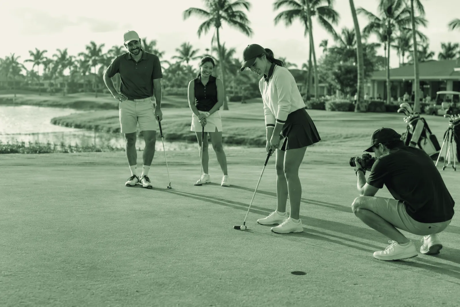 A photographer crouching on a green to film a putt while three other players watch